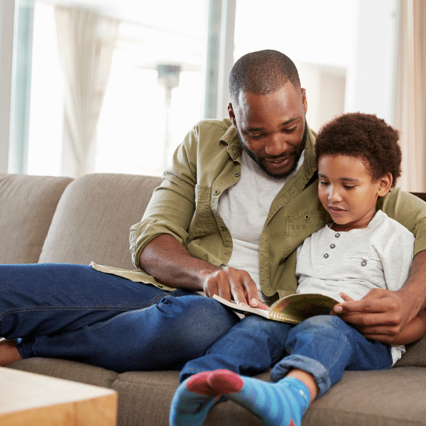 image showing a father reading a book to his son while they are sitting on a couch